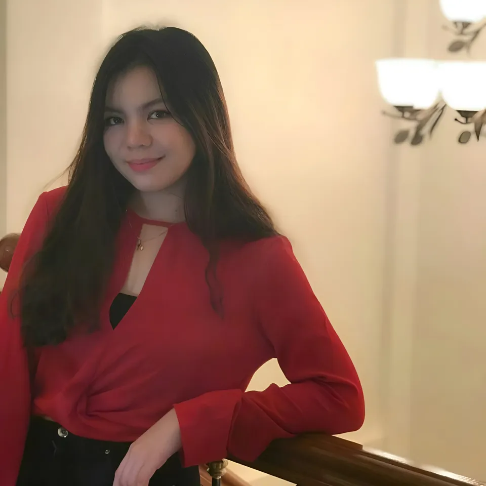 Jeanine Fernandez in red top leaning on wooden railing indoors