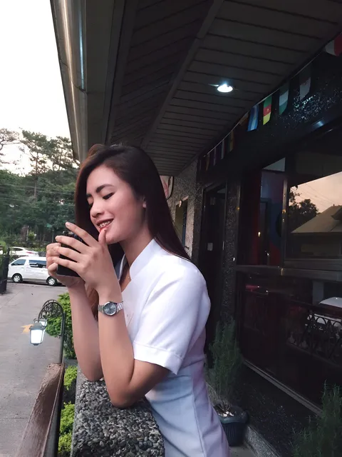 Jenela Tuguinay in white top holding phone outdoors near building