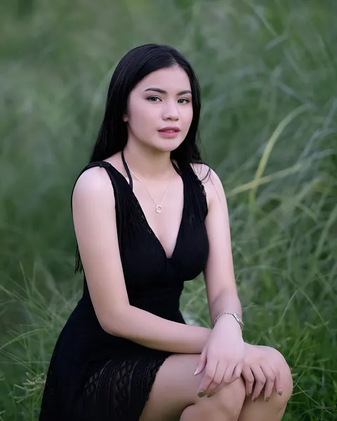 Jennieva Quinn in black dress seated in tall grass