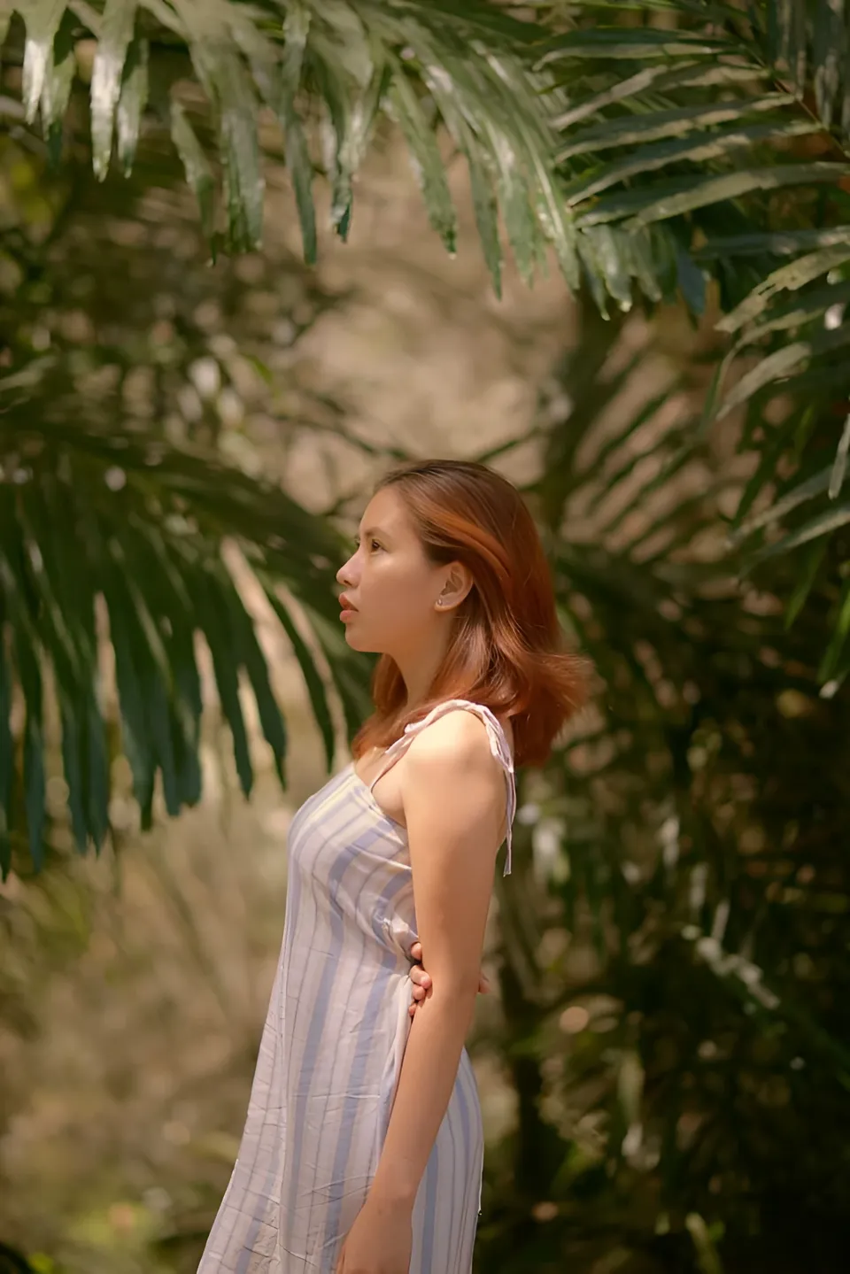 Jessa Bariuan in striped dress standing under palm fronds outdoors