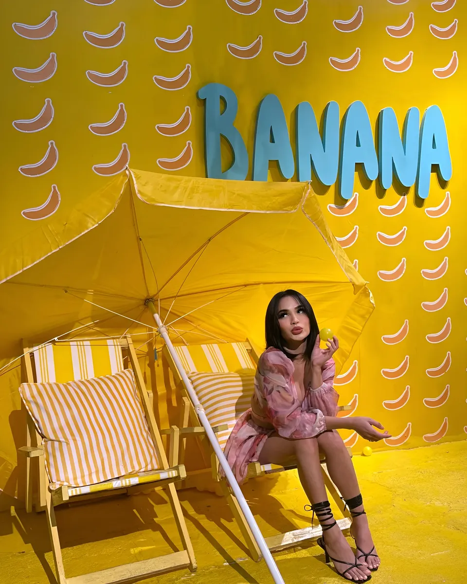 Joey Nerosa in pink floral dress seated under yellow umbrella