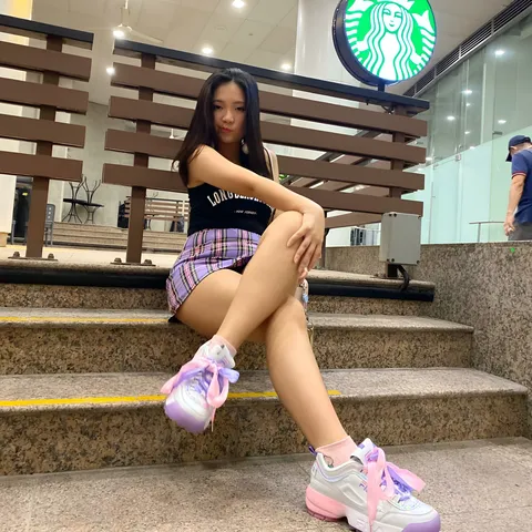 Josie Selene wearing a black top and plaid shorts sits on outdoor steps