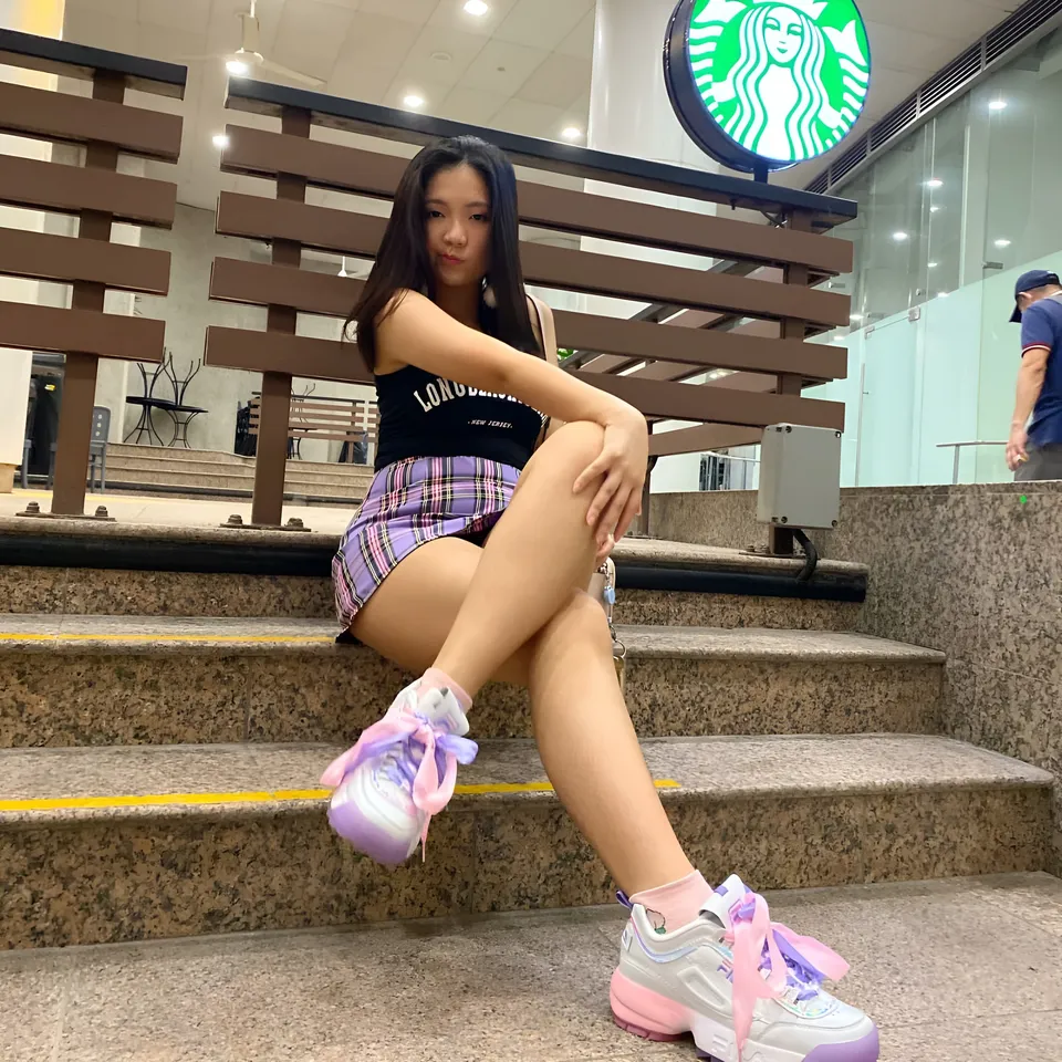 Josie Selene wearing a black top and plaid shorts sits on outdoor steps