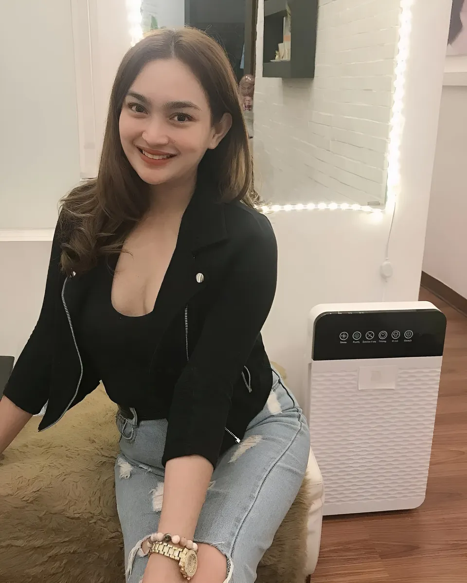 Julia Claire Anne Sotelo in black jacket and jeans sits on cushioned surface