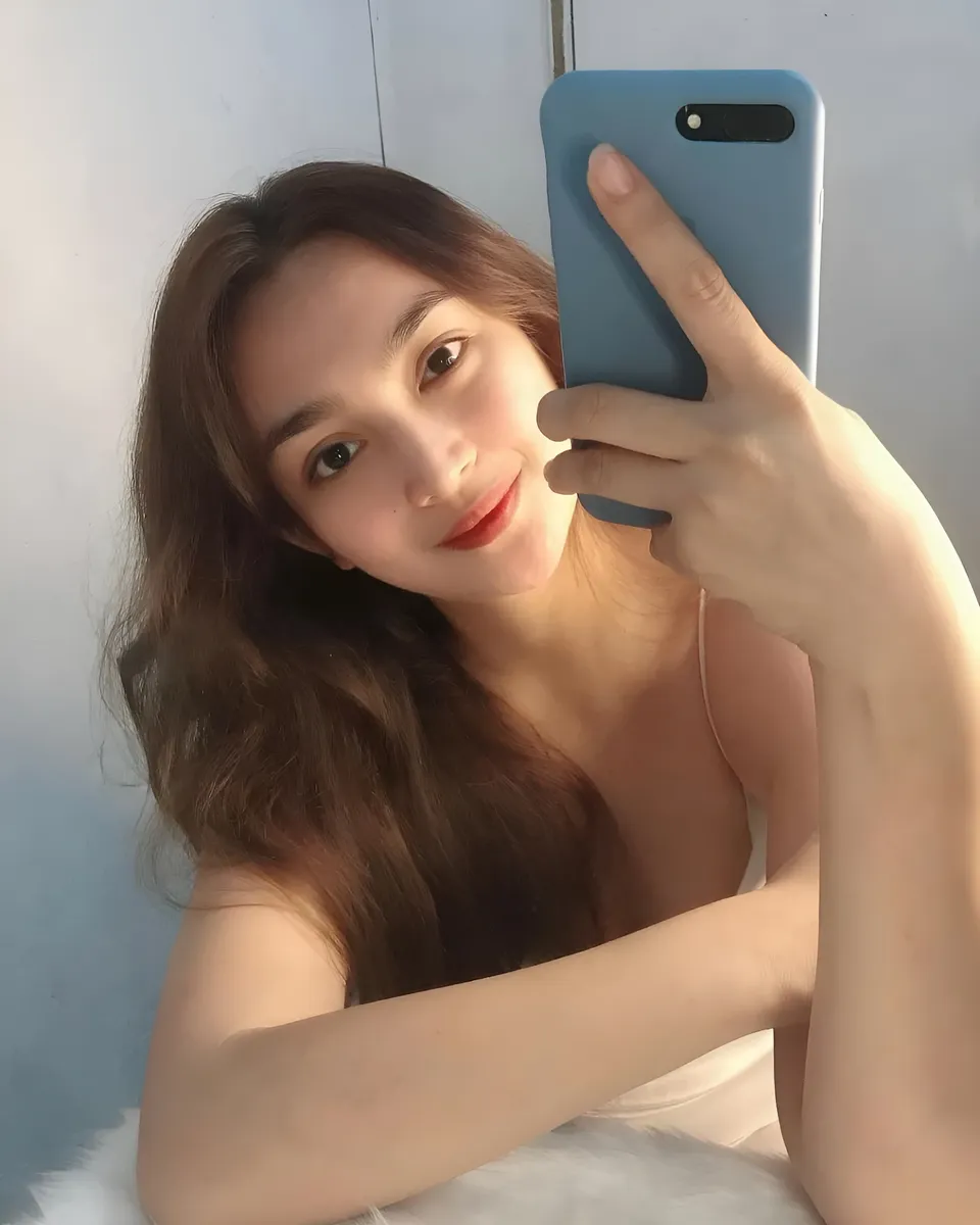 Julia Claire Anne Sotelo taking selfie with blue phone against light wall