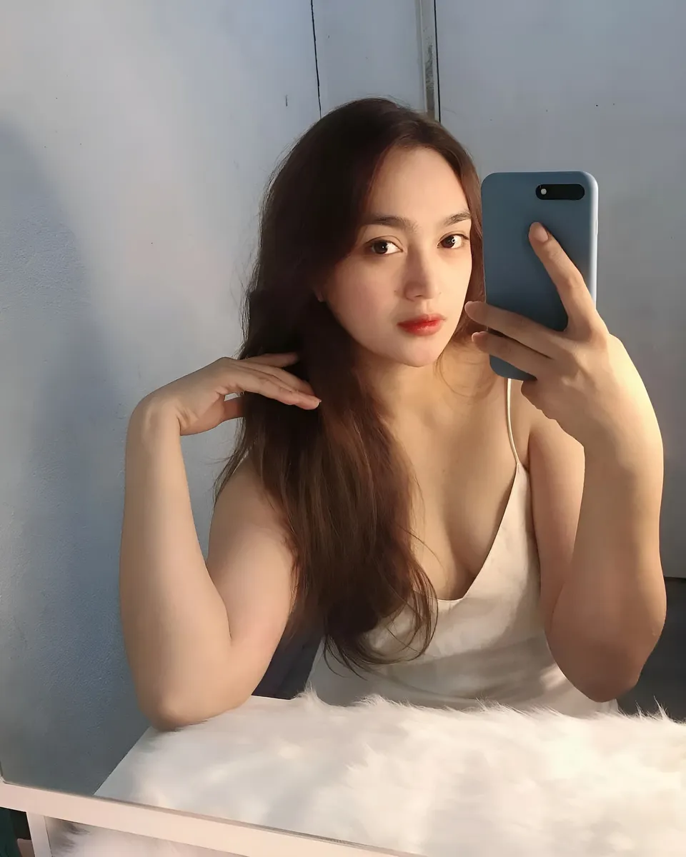 Julia Claire Anne Sotelo taking mirror selfie with phone, wearing white top