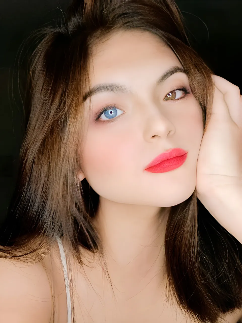 Julia Ostan with blue eyes and red lipstick, hand near face