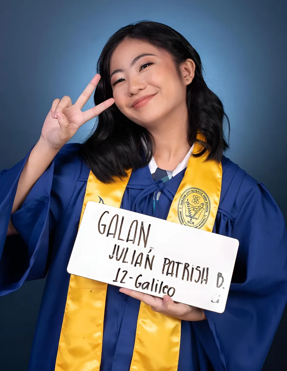 Julian Galan in graduation gown holding white sign with handwritten text