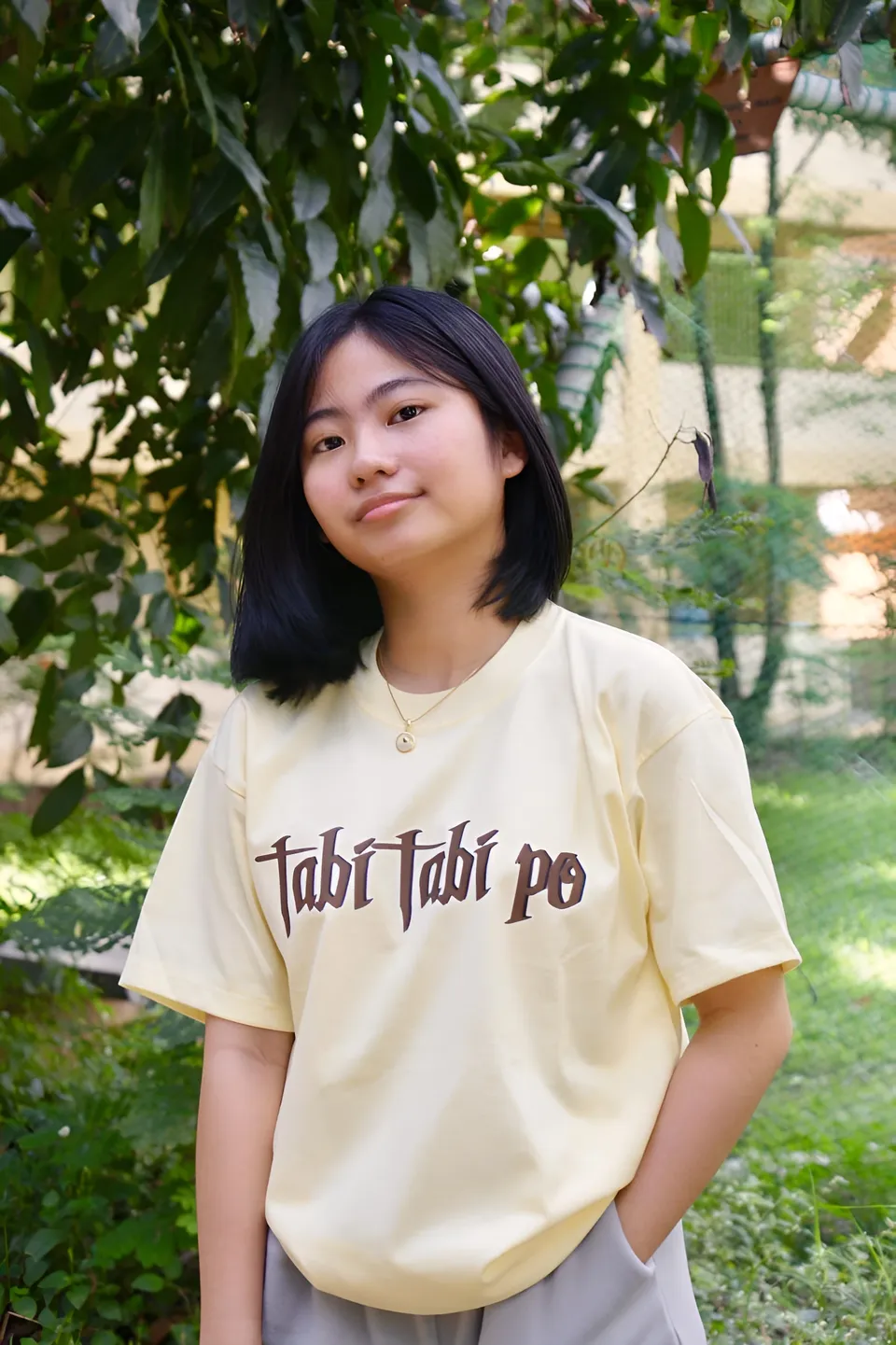 Julian Galan wearing light yellow t-shirt with text under leafy tree