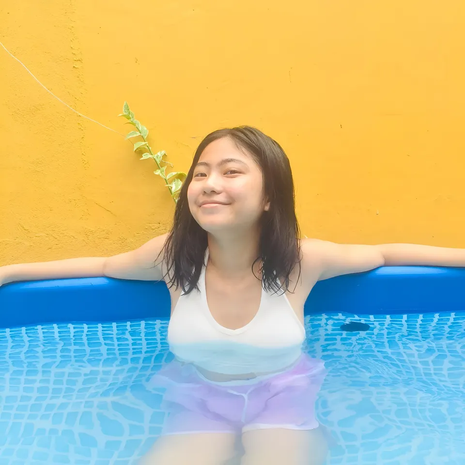 Julian Galan in pool wearing white top and purple shorts, smiling with arms out