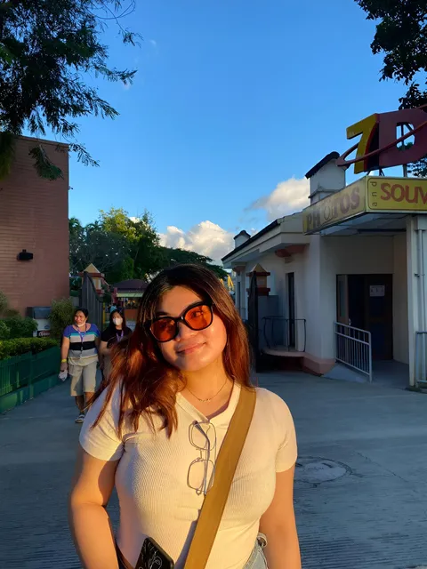 Katherine Bellamy wearing sunglasses and a light top poses on a paved outdoor walkway
