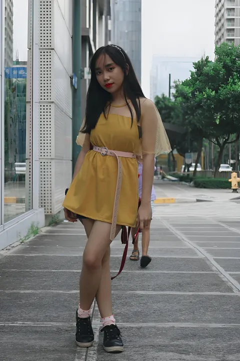 Kathleen Veronica in yellow dress standing on paved street with buildings and trees