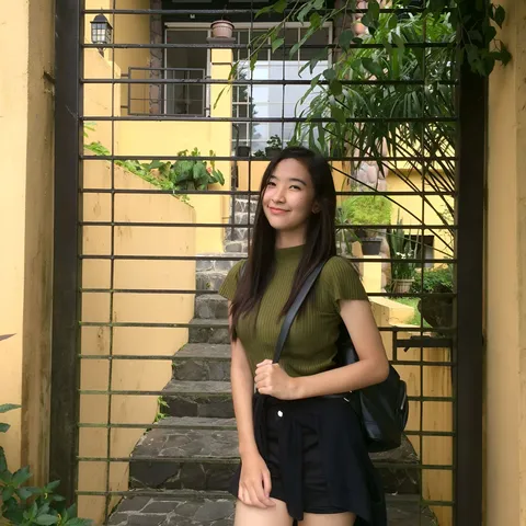 Kayla Cubol wearing a green top and black skirt poses beside a metal gate