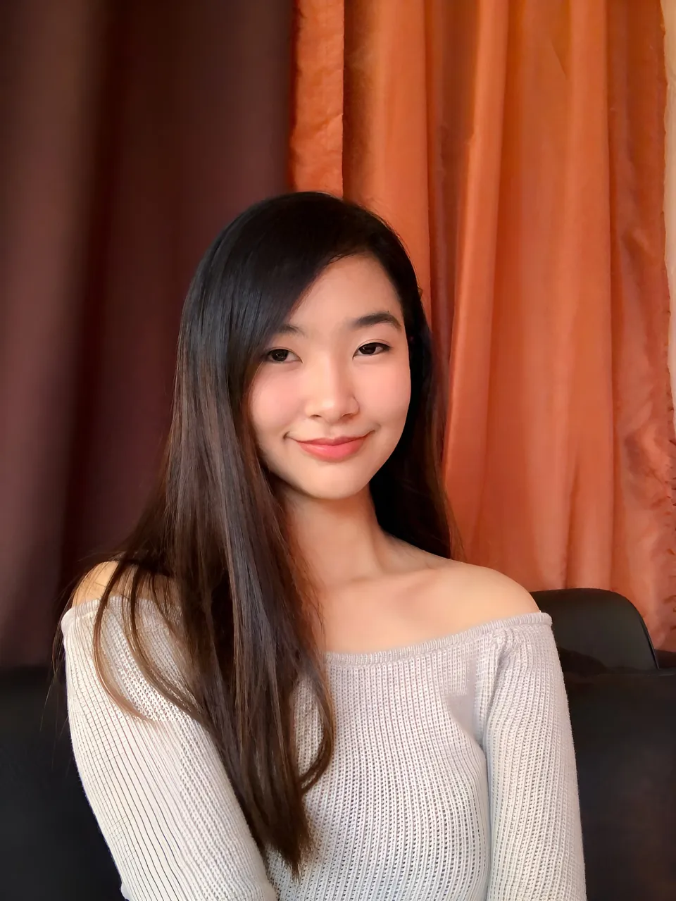 Kayla Cubol in off-shoulder knit top seated in front of curtains