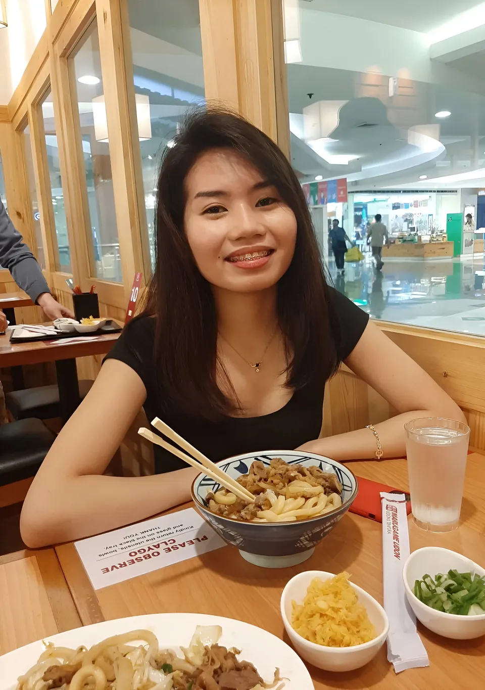 Kim Aubrey Saguinsin wearing a black top smiles at a table with a bowl of noodles