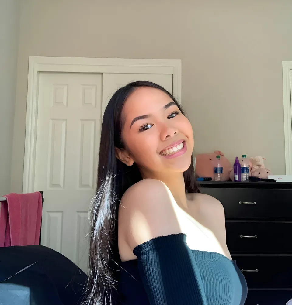 Kobi Ashley smiling in off-shoulder top near dresser and door