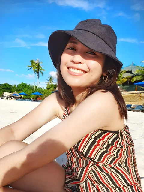 Kokies Lim in striped top and hat sitting on beach