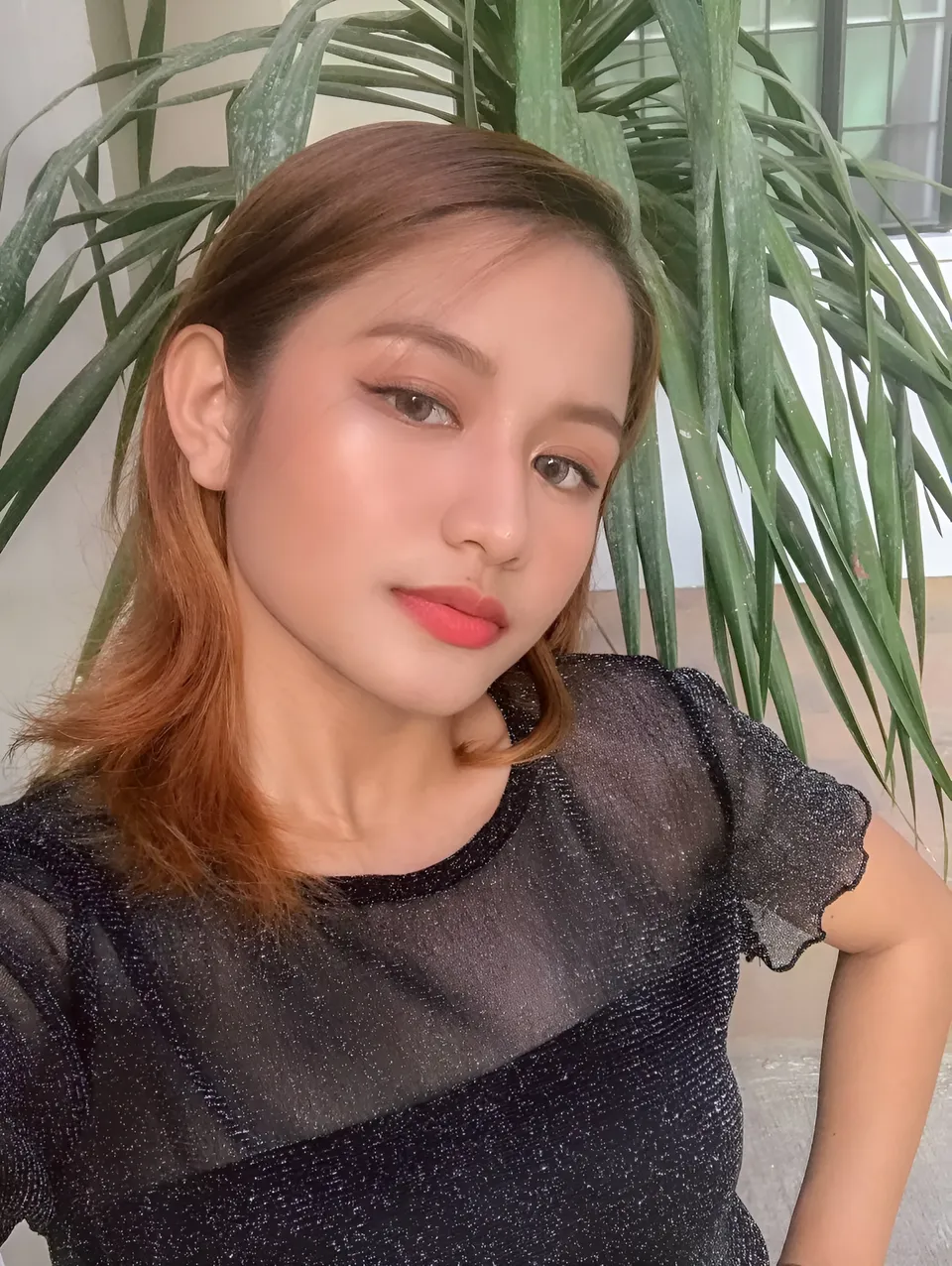 Krysta Matias in black sparkly top poses with green plant behind her