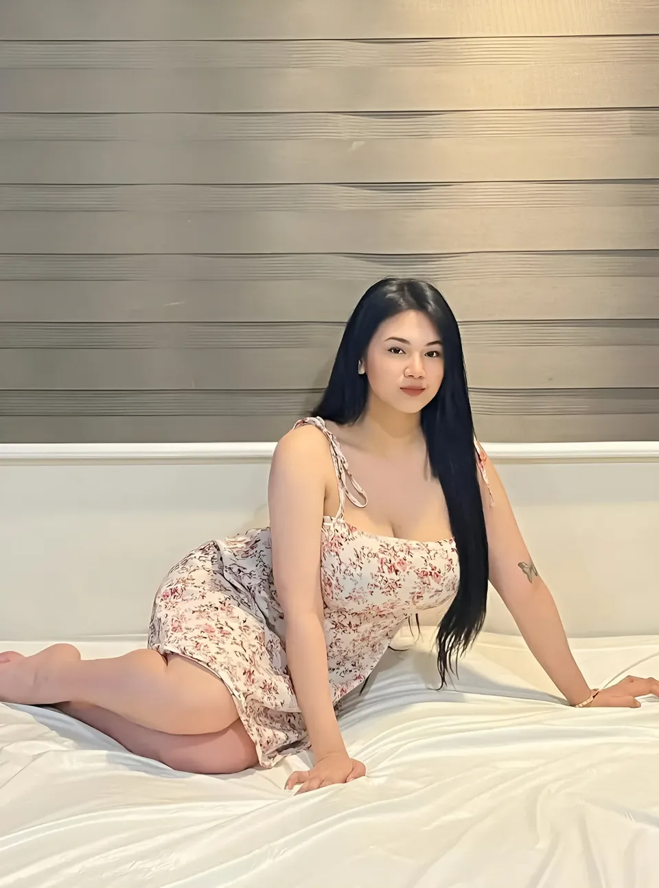 Kyla Westbrook in floral dress sitting on bed with striped wall background