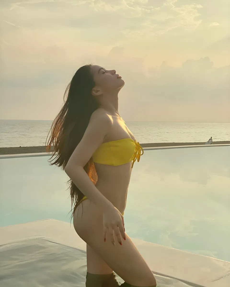 Lhyn Ampong in yellow bikini top standing by pool at sunset