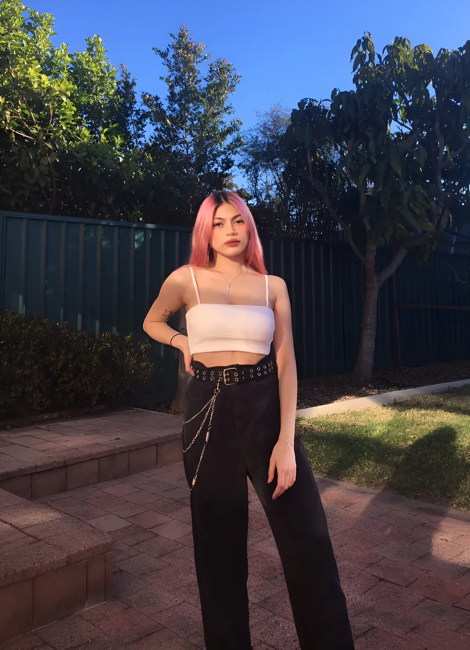 Lia Mae Vumbaca with pink hair stands outdoors in white top and black pants