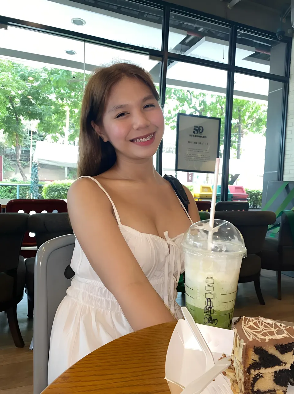 Love Dela Pe in white top seated at table with drink and cake