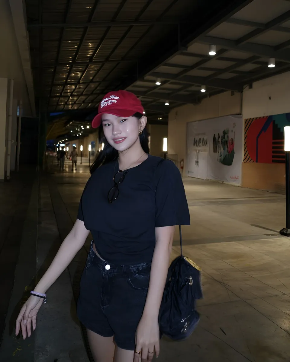 Maeve Linden in black top and shorts stands in illuminated indoor corridor