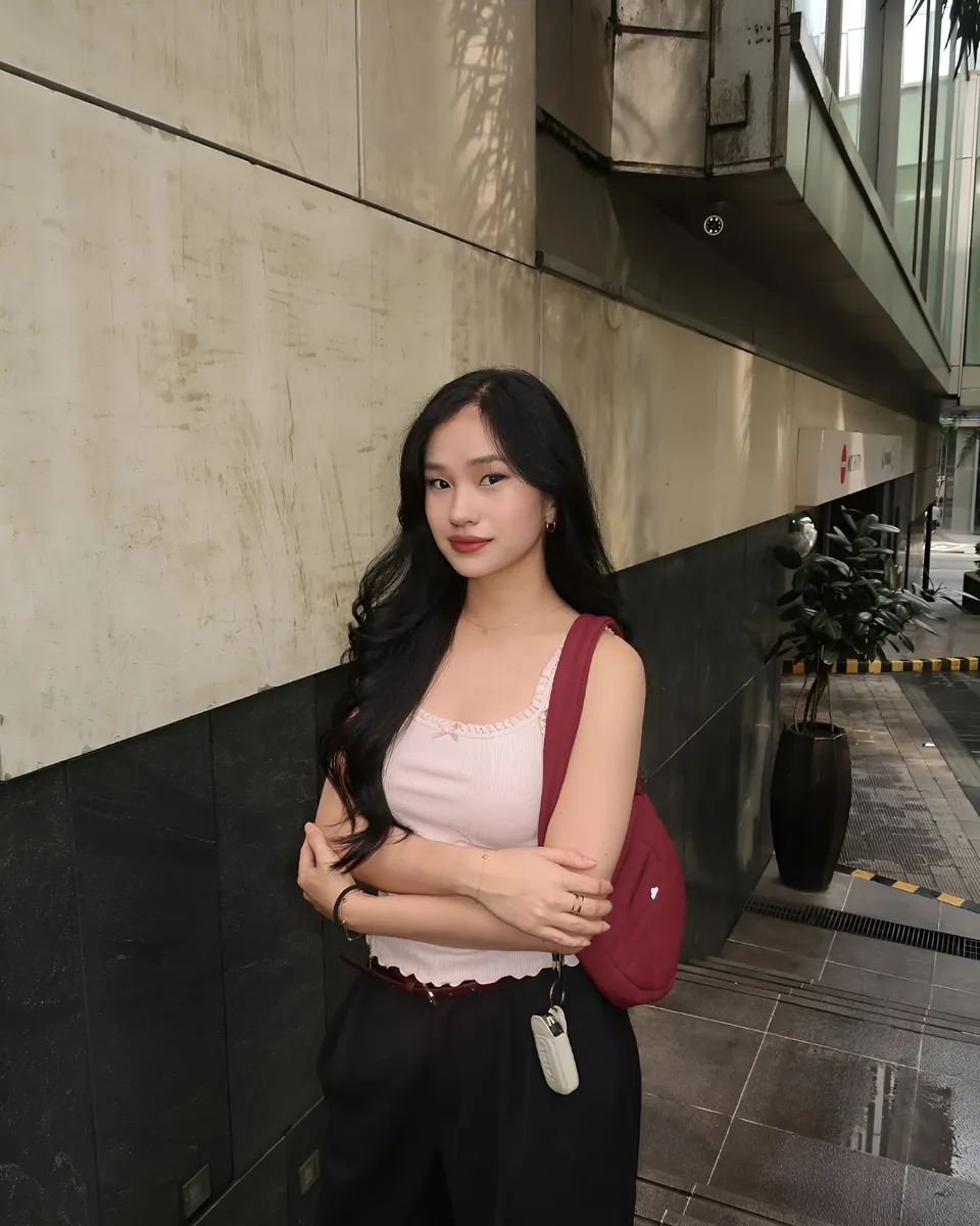 Maeve Linden in pink top and dark pants stands with arms crossed against a wall