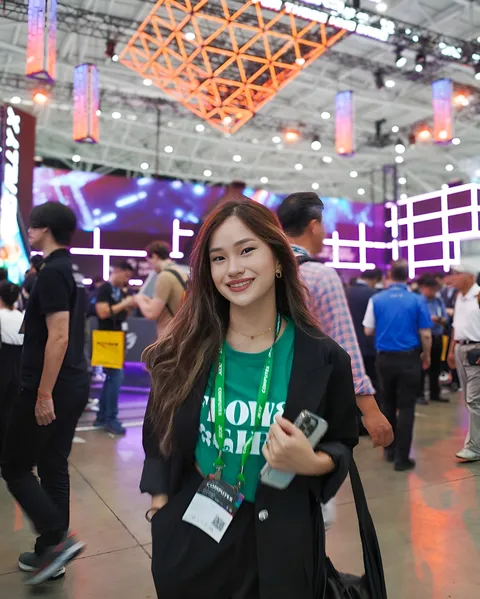 Maeve Linden smiling in convention hall wearing green shirt and black jacket