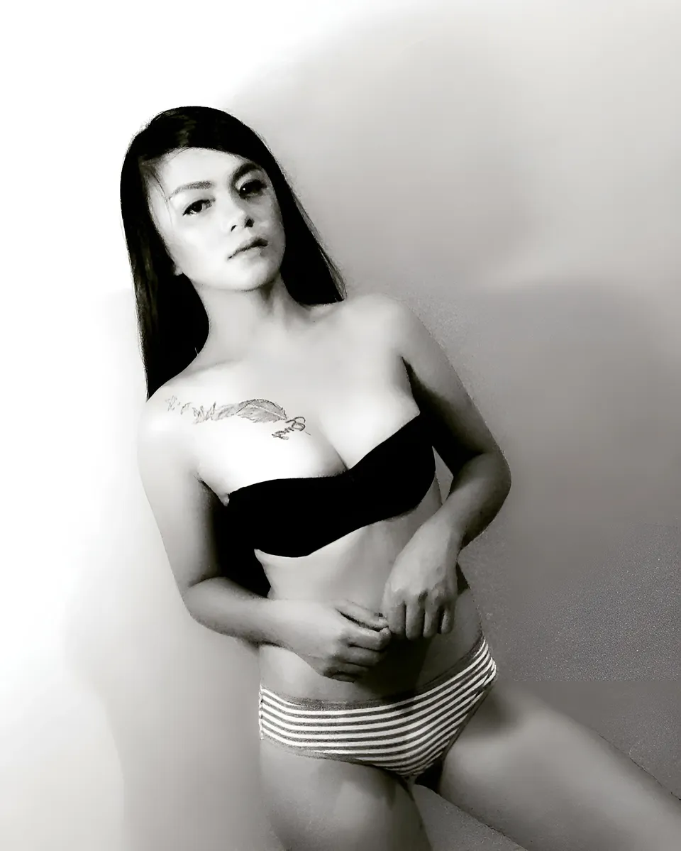 Margielyn Nocum in black bra and striped underwear leaning against wall