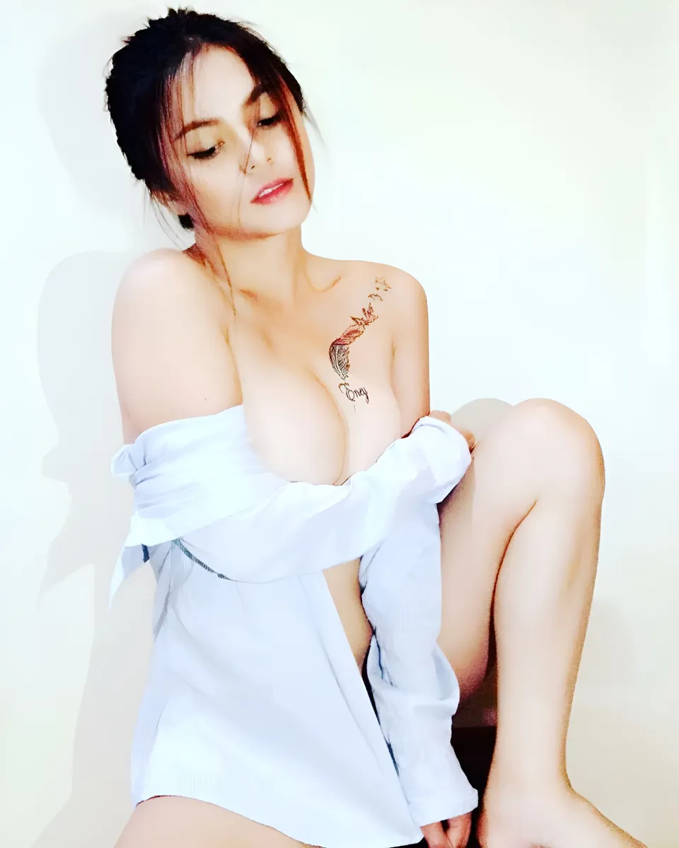 Margielyn Nocum wearing an open white shirt poses seated against a light background