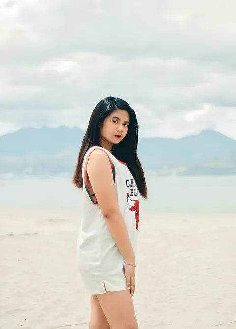 Maria Dacayo in white top standing on sandy beach with mountains in background