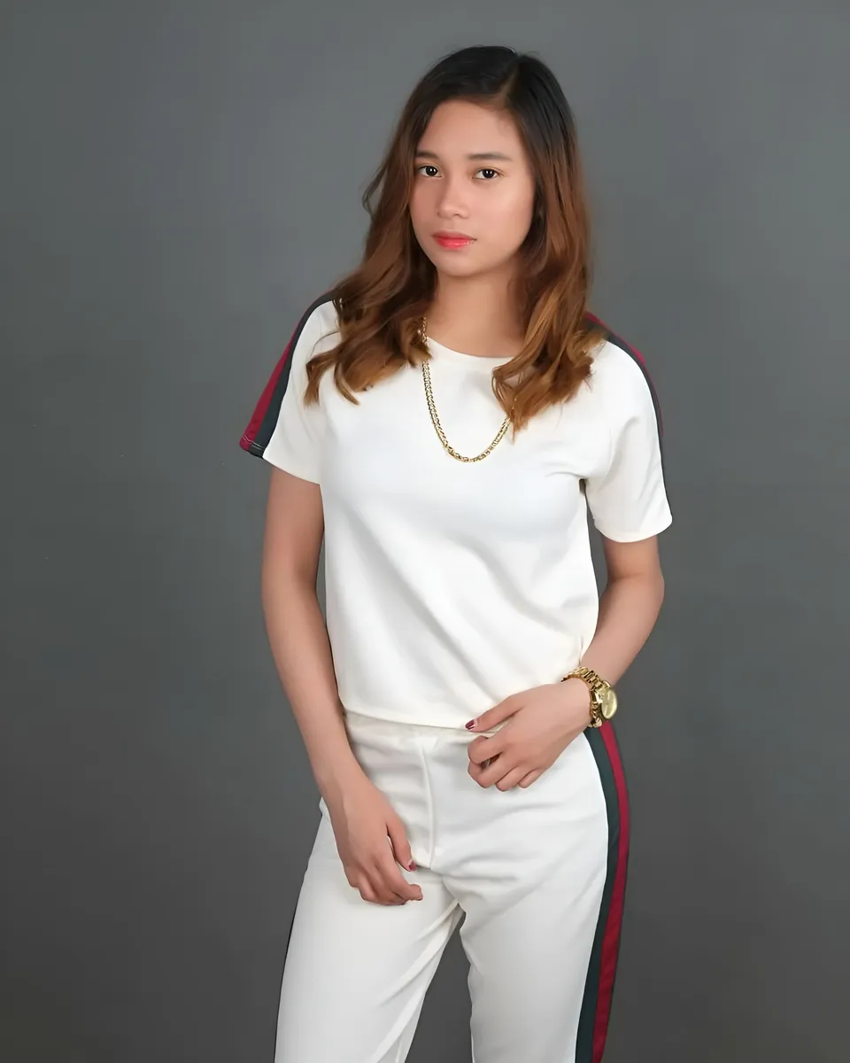 Marries Cabral wearing a white top and striped white pants poses against a plain wall