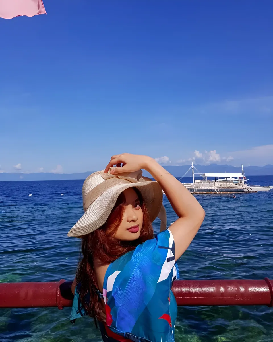 Mary Therese Rizon in blue patterned top stands by railing overlooking ocean