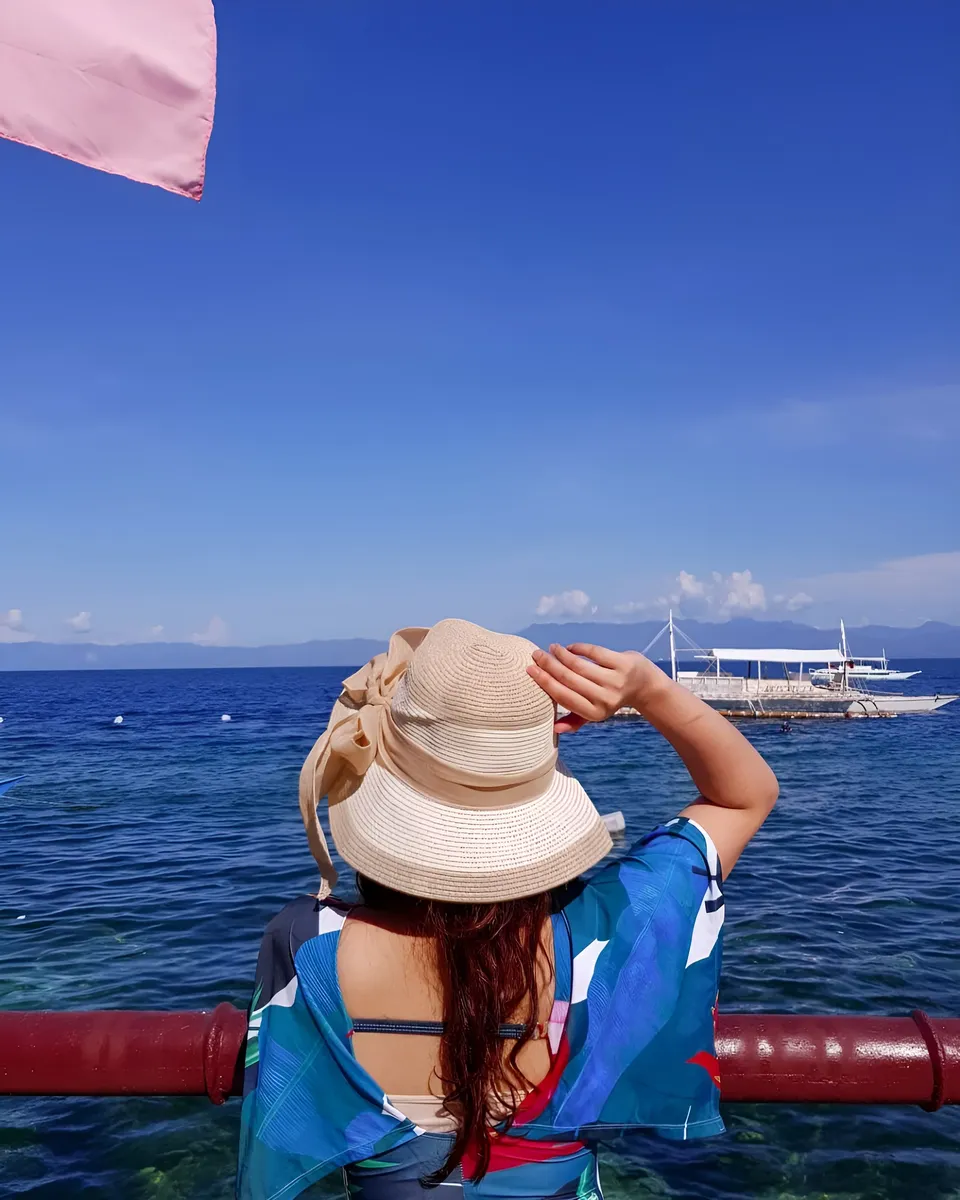 Mary Therese Rizon wearing hat and colorful top overlooking ocean with boat