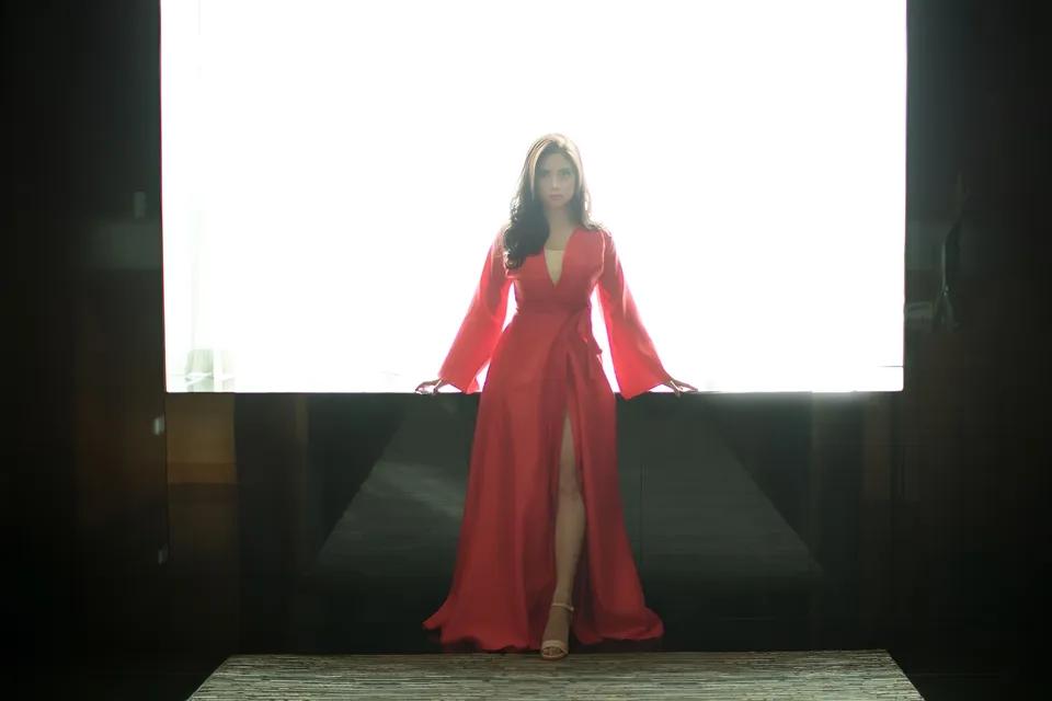 Mary Therese Rizon in red gown standing before bright window