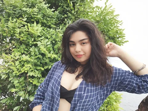 Merryl Nestor wearing an open blue plaid shirt poses in front of green foliage