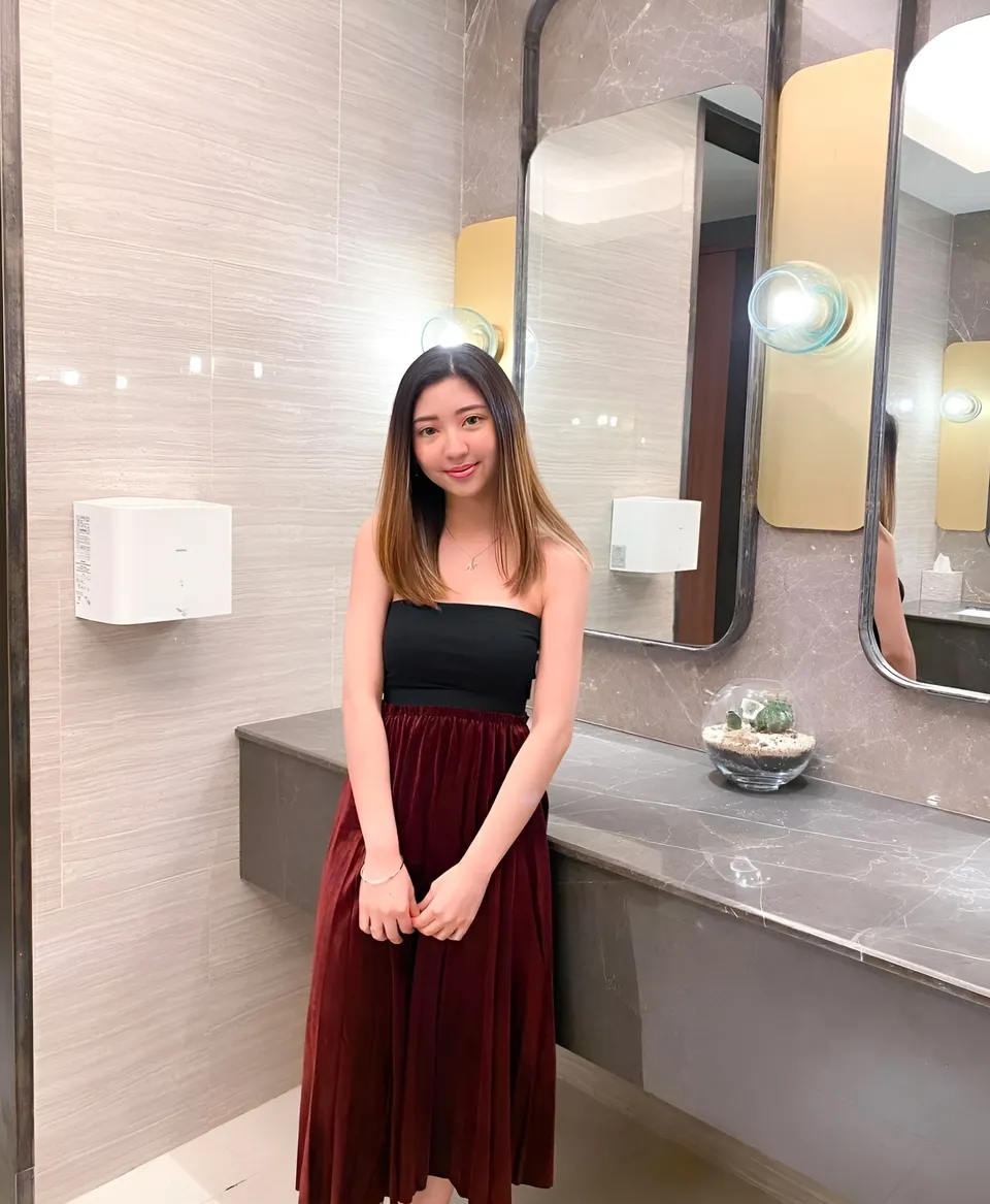 Michelle Arden in black top and red skirt stands in bathroom