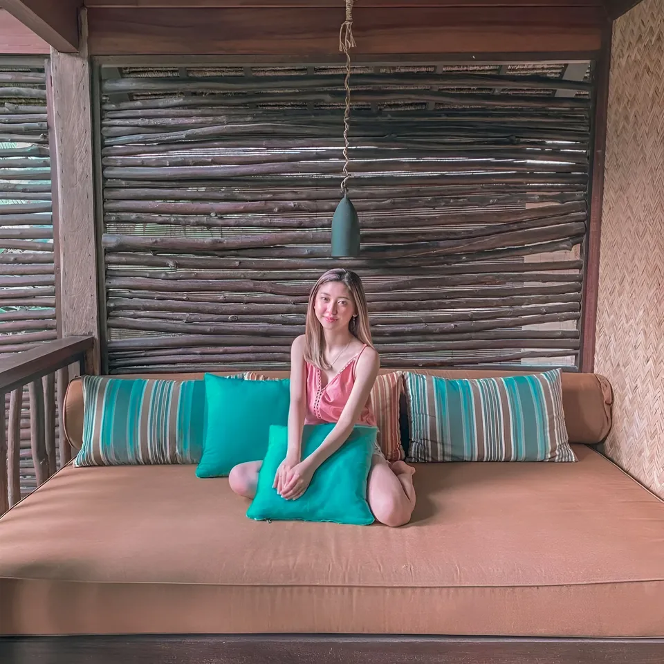 Michelle Arden sits on cushioned bench with striped pillows under wooden slat wall