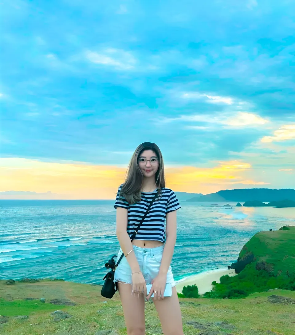 Michelle Arden in striped shirt stands on grassy cliff overlooking ocean