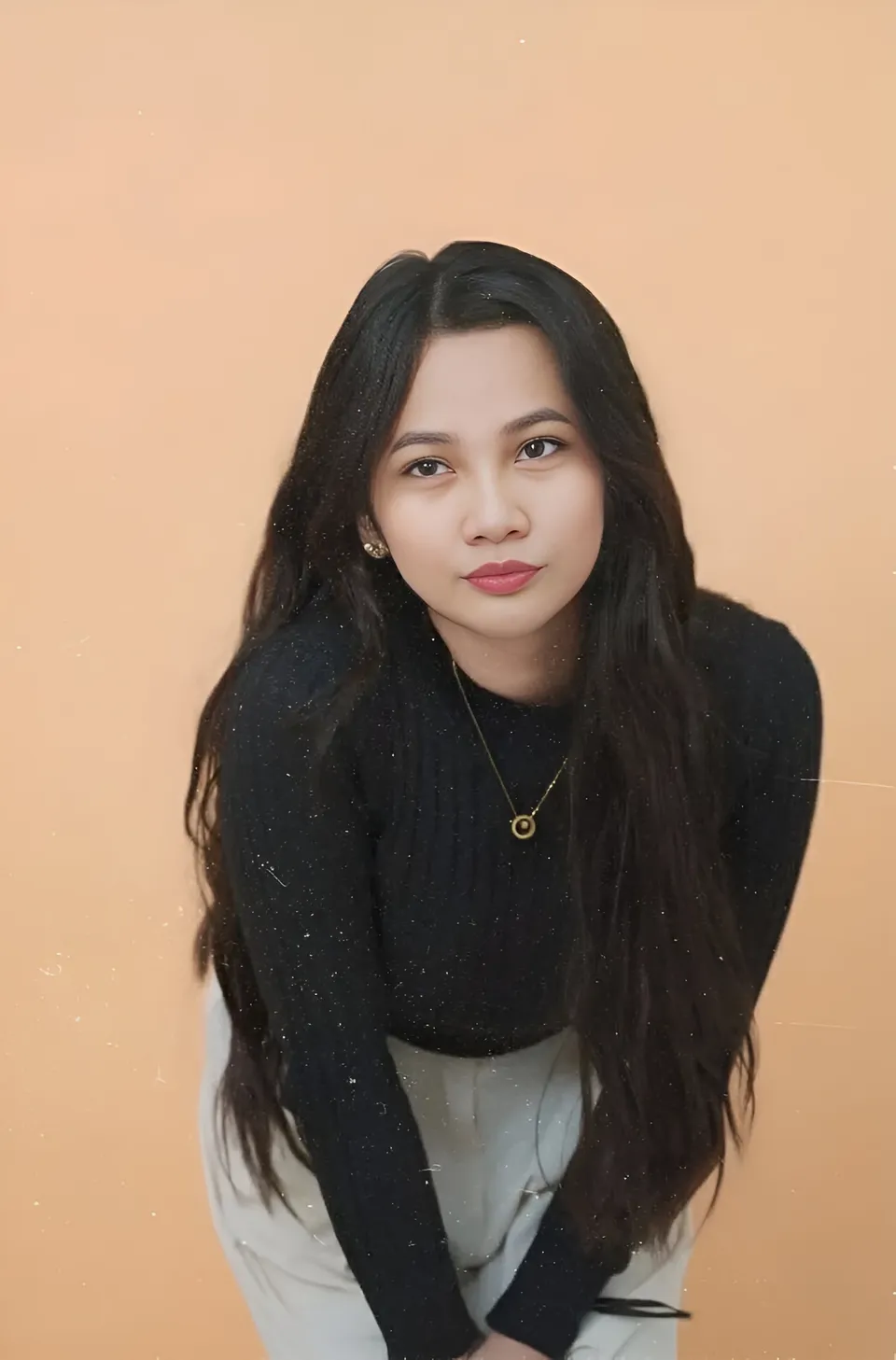 Mikay Alexis in black top and light pants seated against peach background