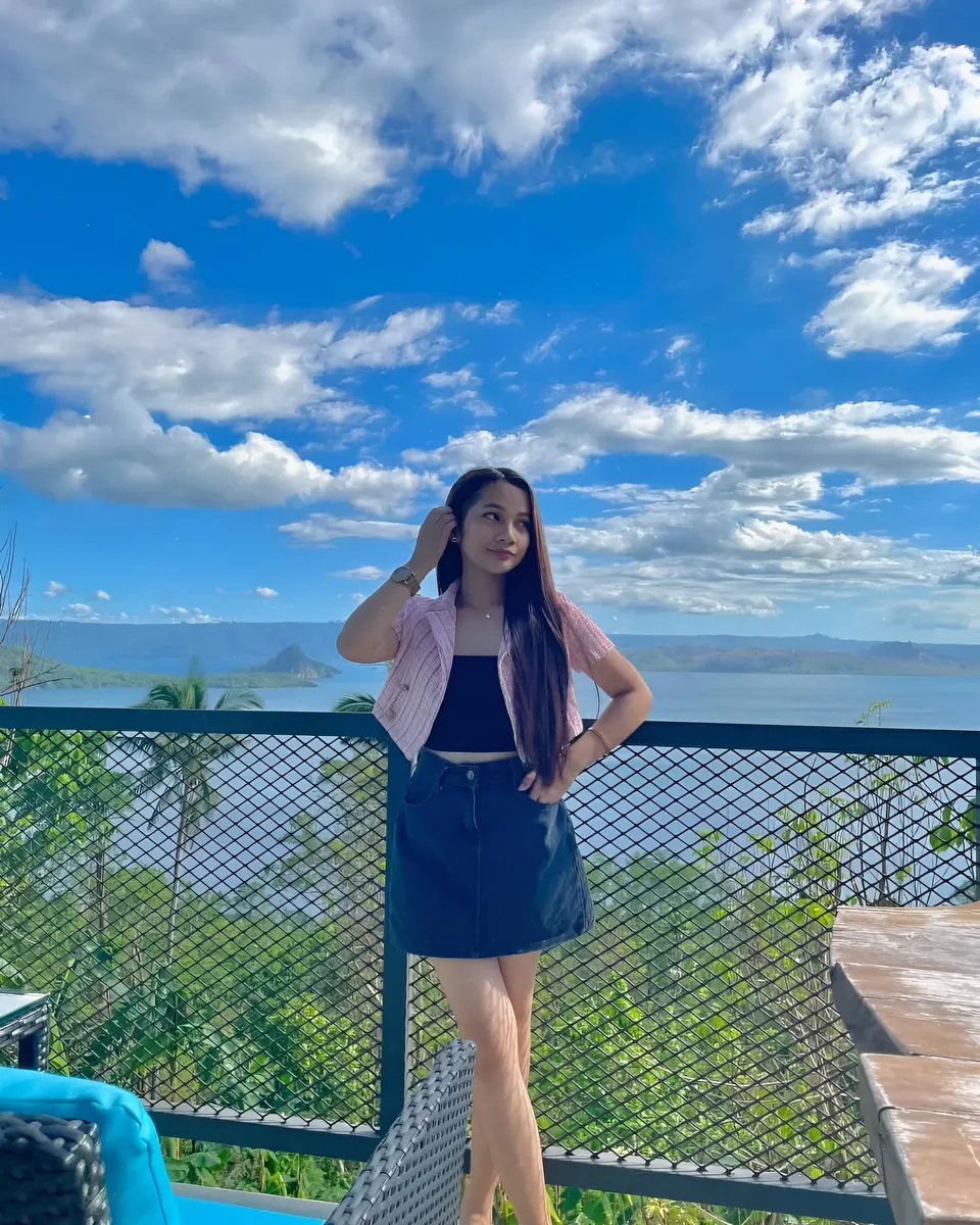Mikay Alexis in pink jacket stands on balcony overlooking water and hills
