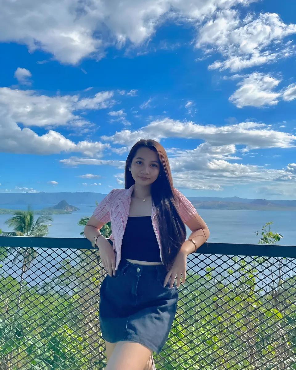 Mikay Alexis in pink jacket stands by railing overlooking water and sky