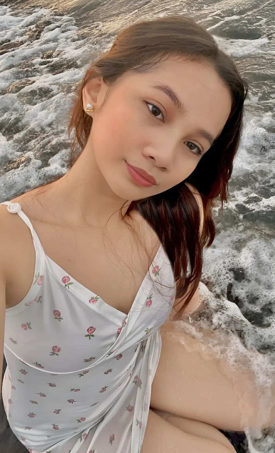 Mikay Alexis in white floral top seated by ocean waves