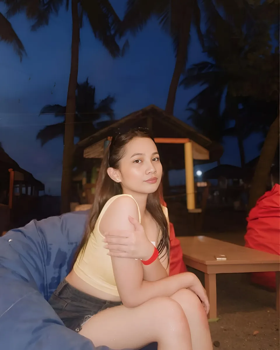 Mikay Alexis in yellow top seated on blue cushion outdoors at dusk