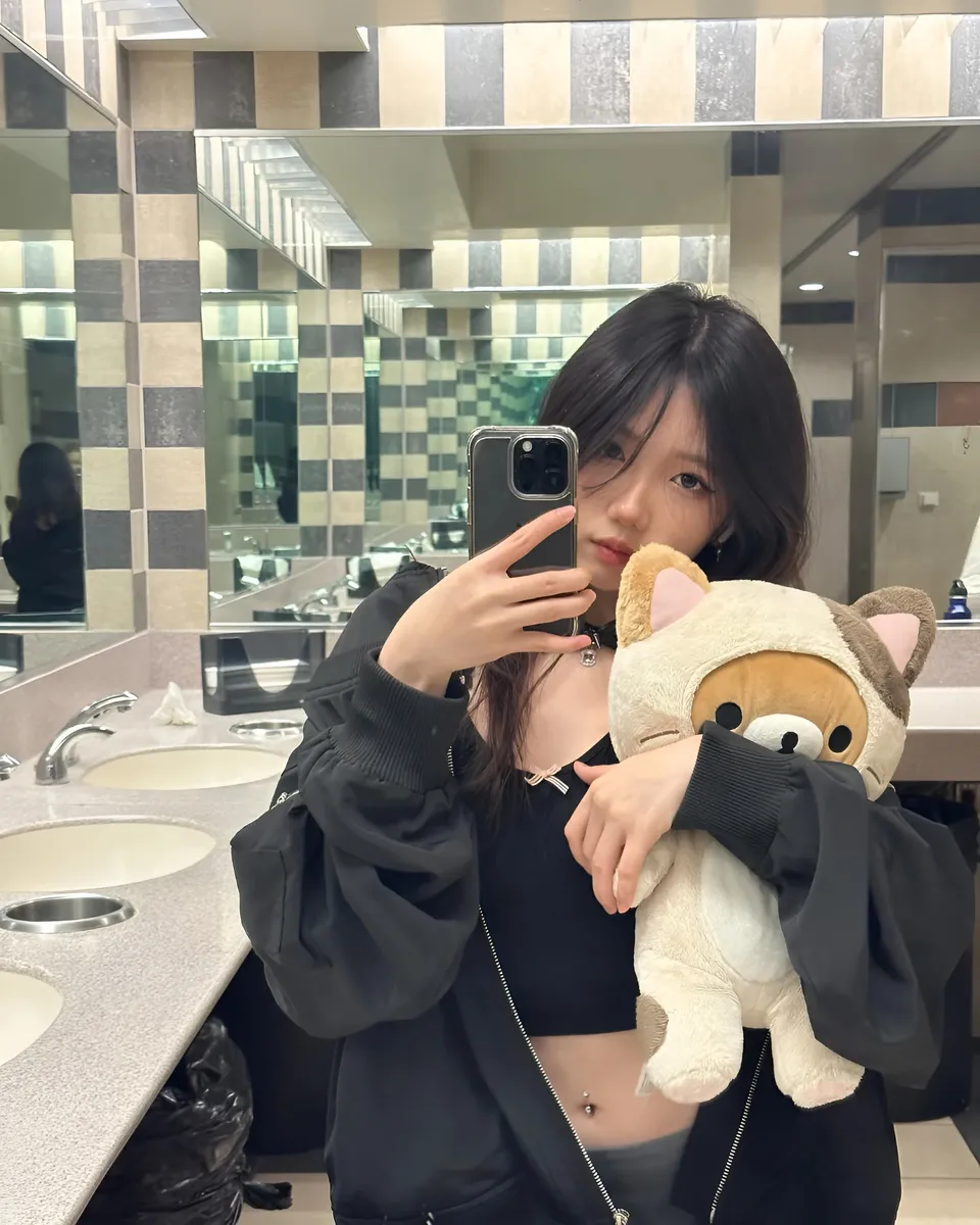 Mina Hartley holding plush toy in bathroom mirror selfie