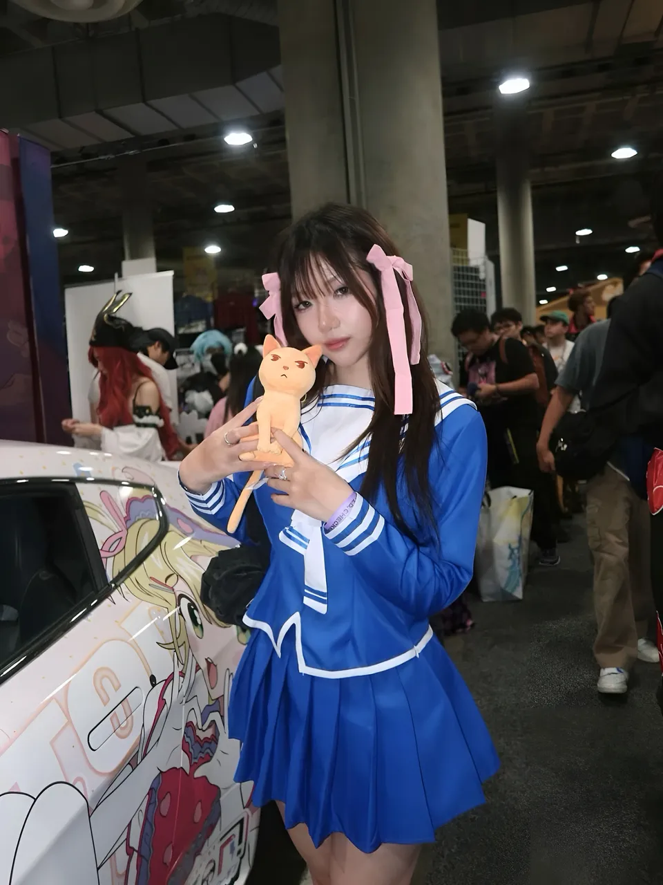 Mina Hartley in blue sailor outfit holds orange cat plush near car