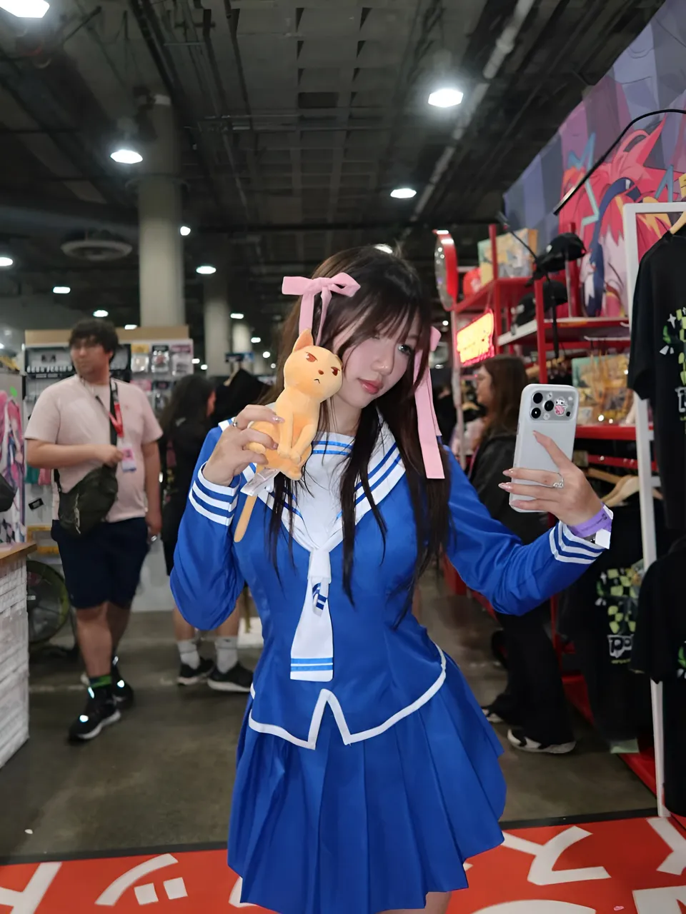 Mina Hartley in blue sailor outfit holds plush toy while taking selfie at convention