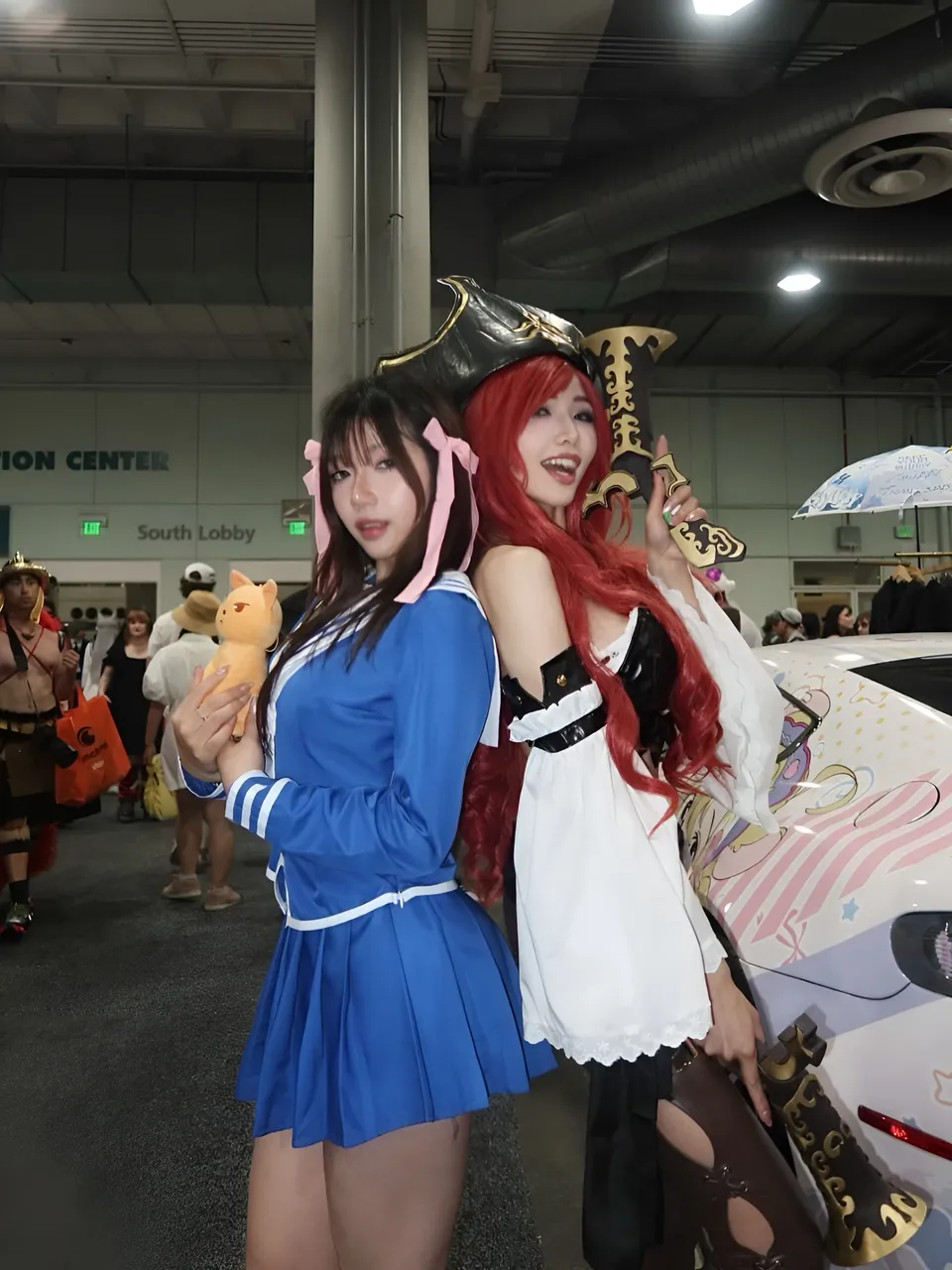 Mina Hartley — Two cosplayers pose beside a decorated car at convention center