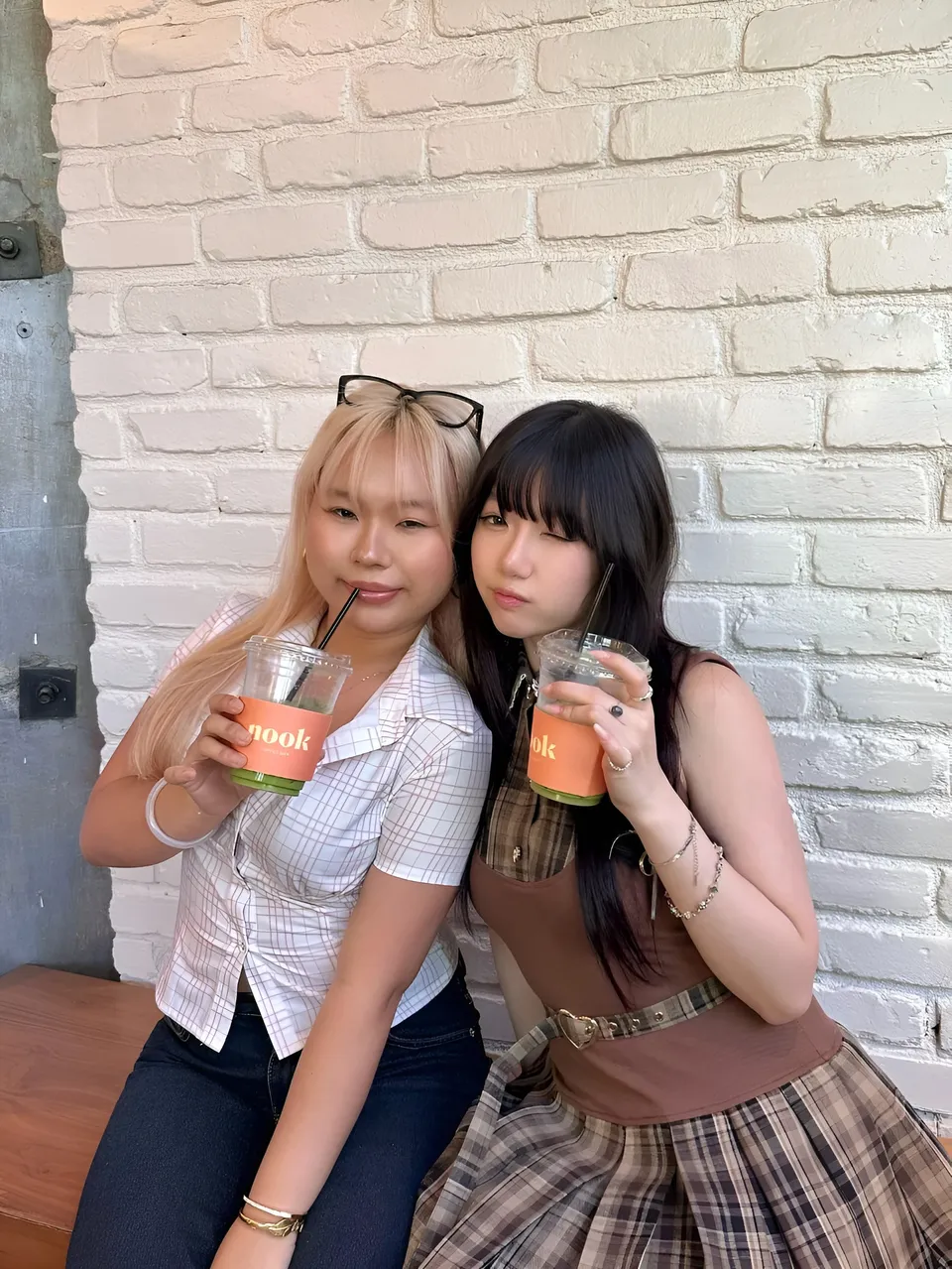 Mina Hartley — Two people holding drinks against white brick wall